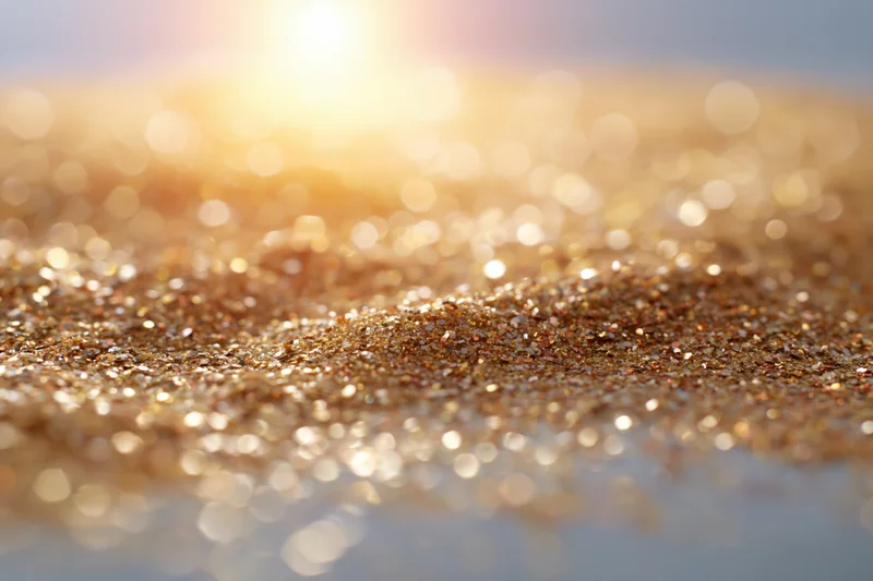 Scattered golden glitter particles on a textured surface with bokeh light reflections in the background