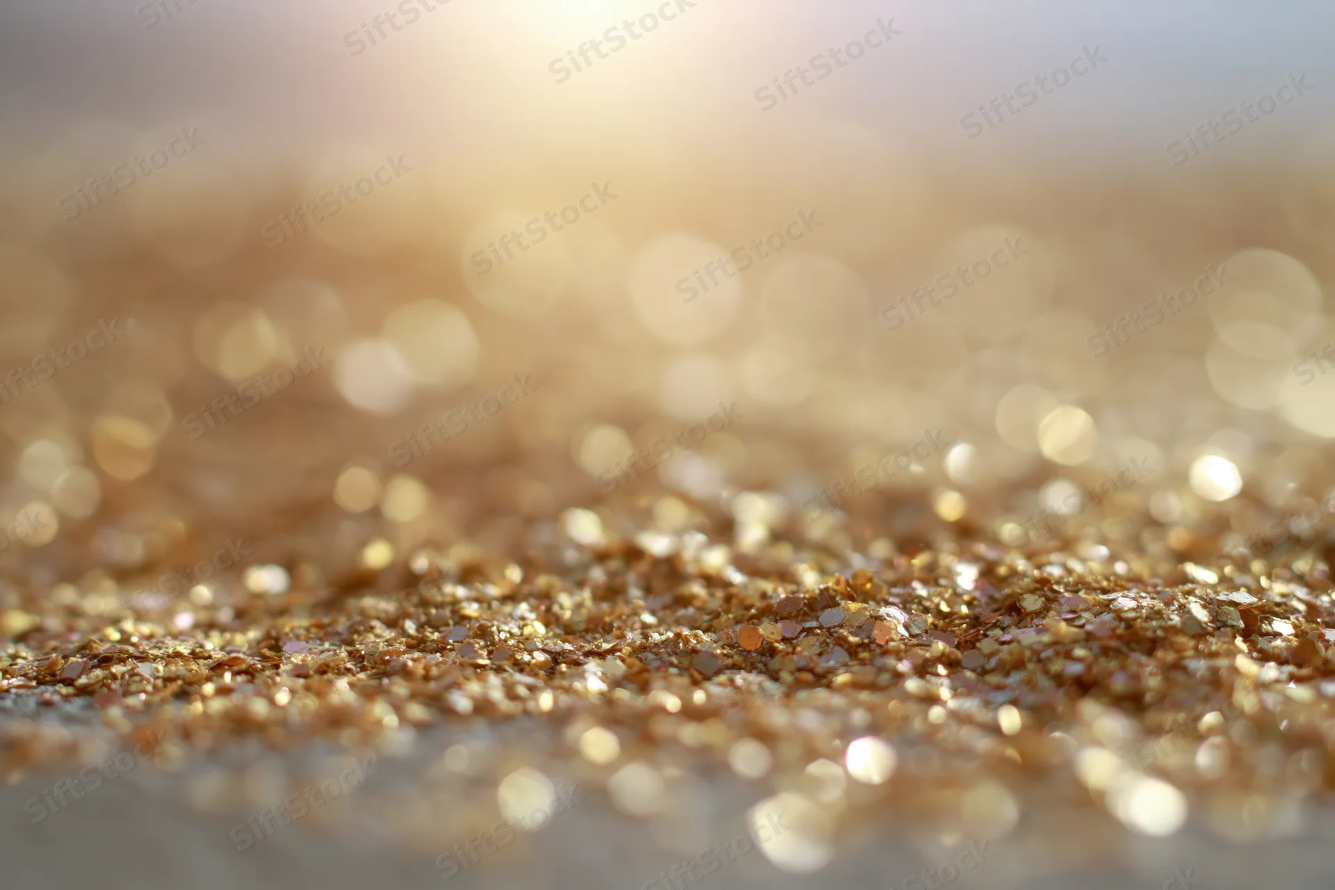 Scattered golden glitter particles on a surface with bokeh light reflections in the background