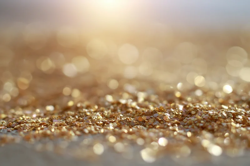 Scattered golden glitter particles on a surface with bokeh light reflections in the background