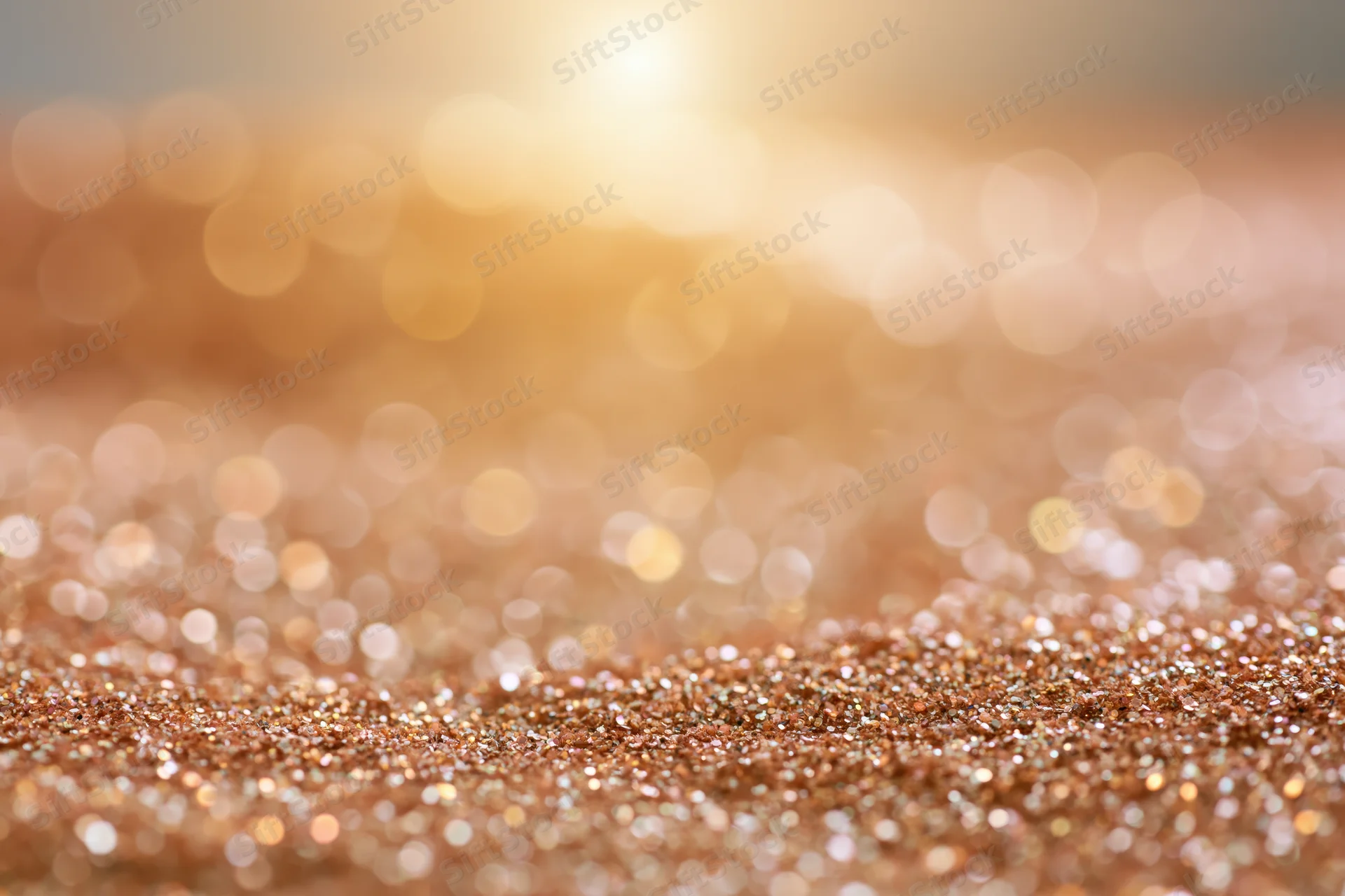 Glittering gold particles scattered across a soft blurred surface with warm bokeh lights in the background
