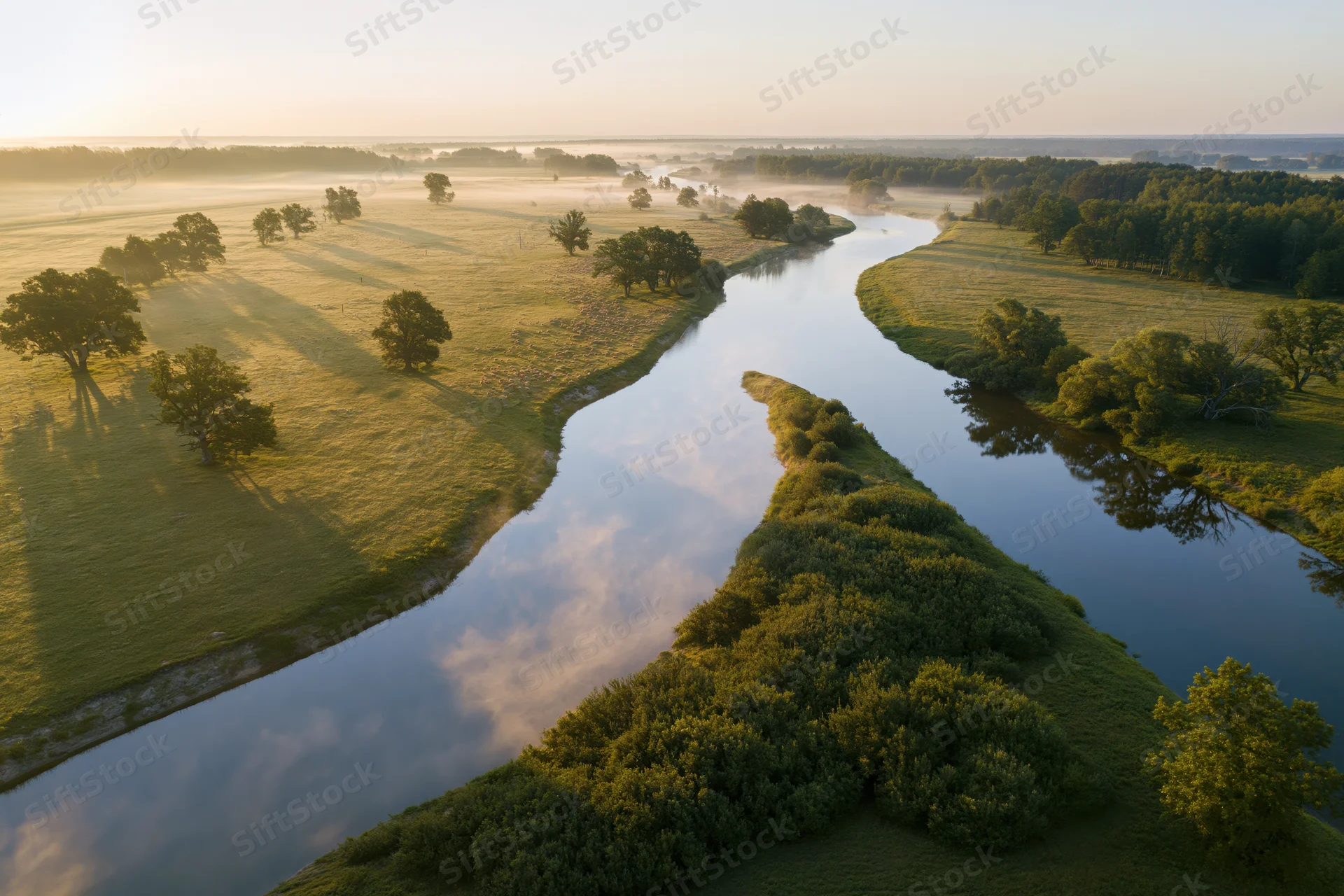 Winding river reflecting sky and clouds through green meadows at sunrise