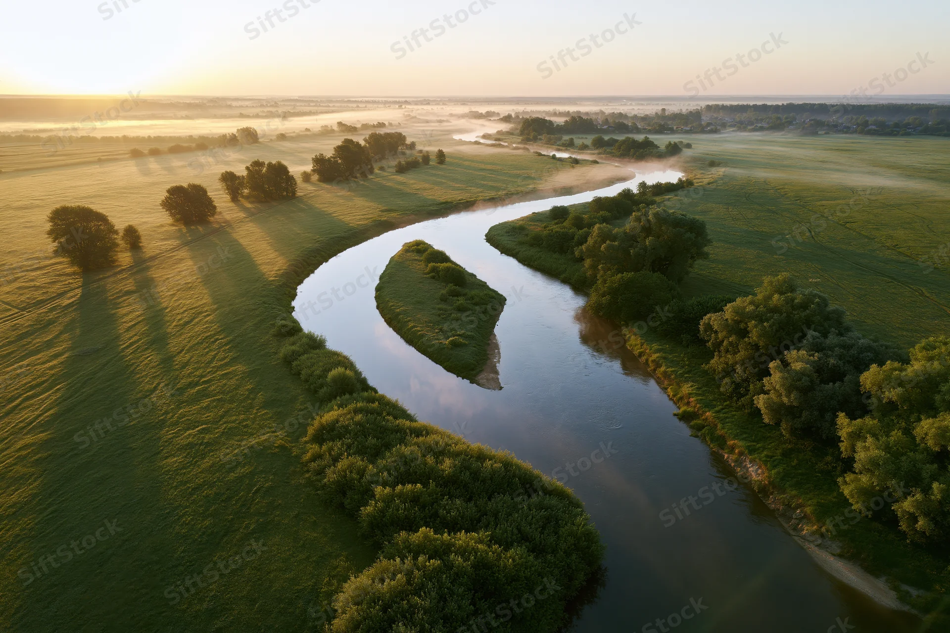 Winding river snaking through flat green meadow at sunrise