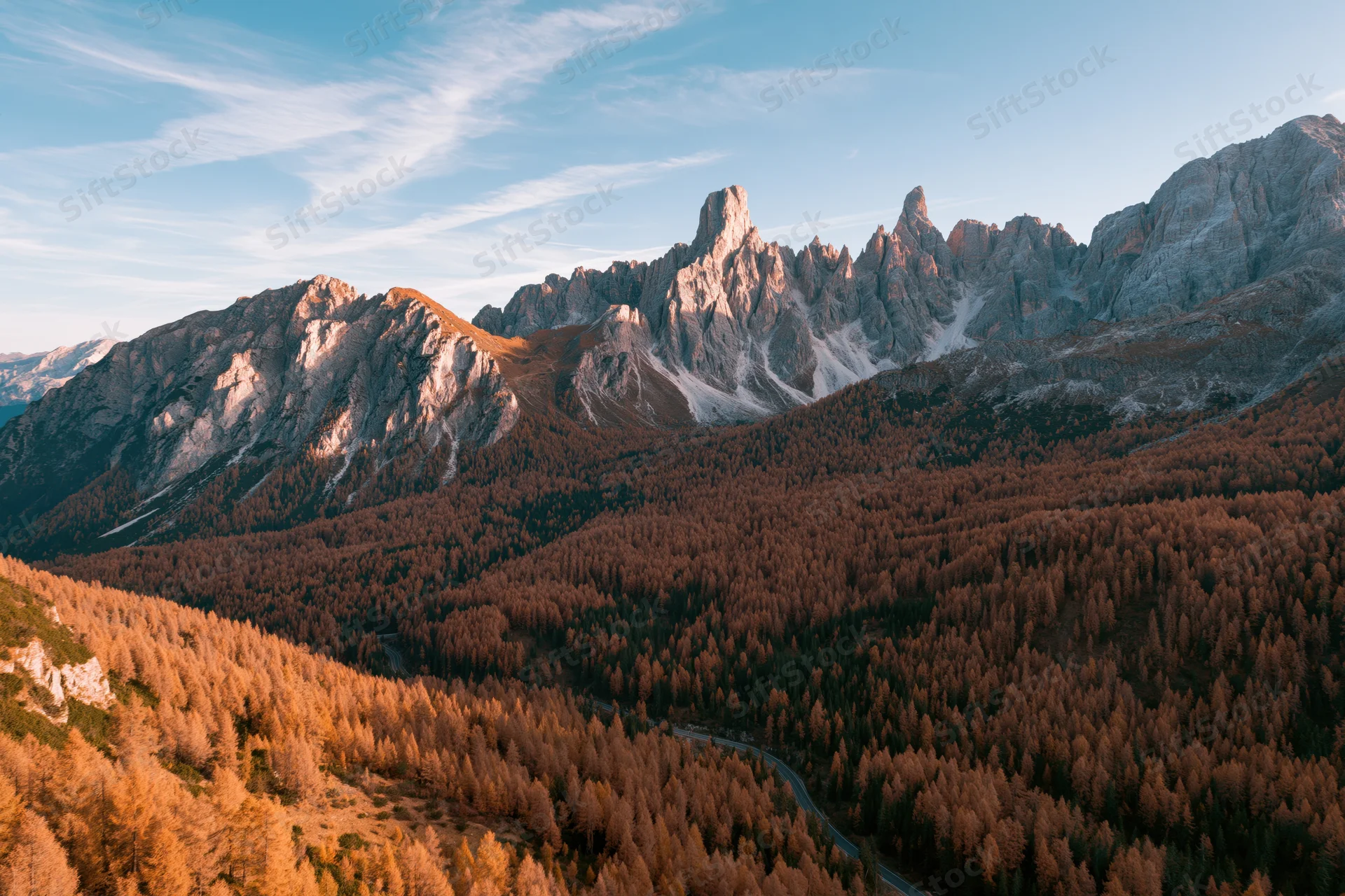 Aerial view of jagged dolomite peaks above autumn forest valley with winding road