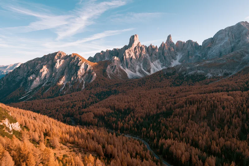 Aerial view of jagged dolomite peaks above autumn forest valley with winding road