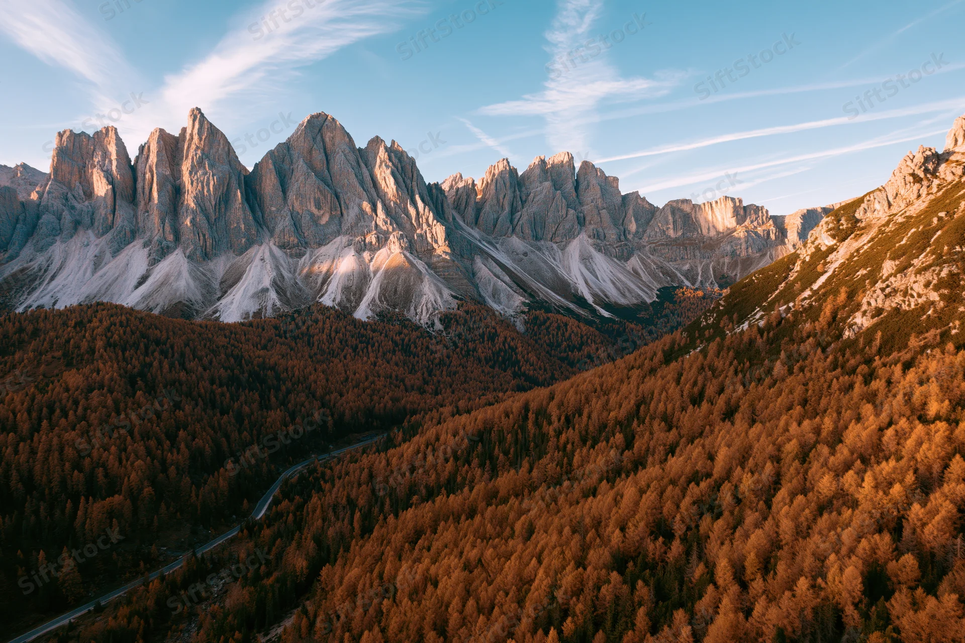 Aerial view of jagged dolomite peaks above autumn forest valley with winding road