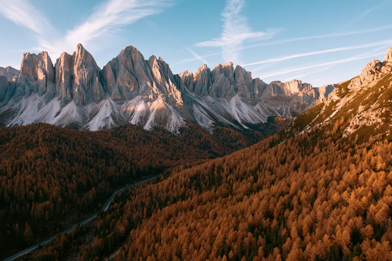 Aerial view of jagged dolomite peaks above autumn forest valley with winding road