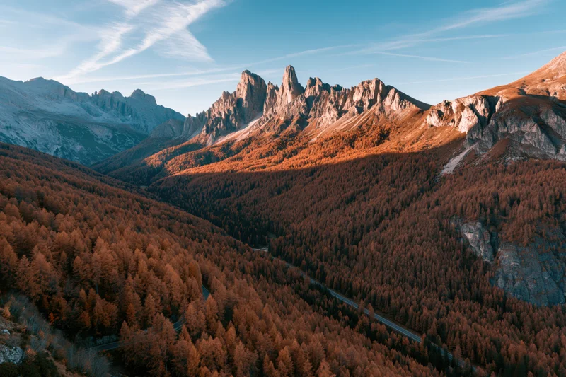Aerial view of jagged rocky peaks and autumn-colored larch forest in the dolomites valley