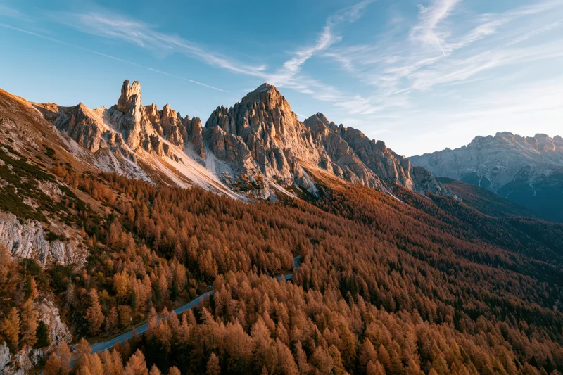 Aerial view of jagged rocky peaks and golden larch forest in the dolomites during autumn sunset