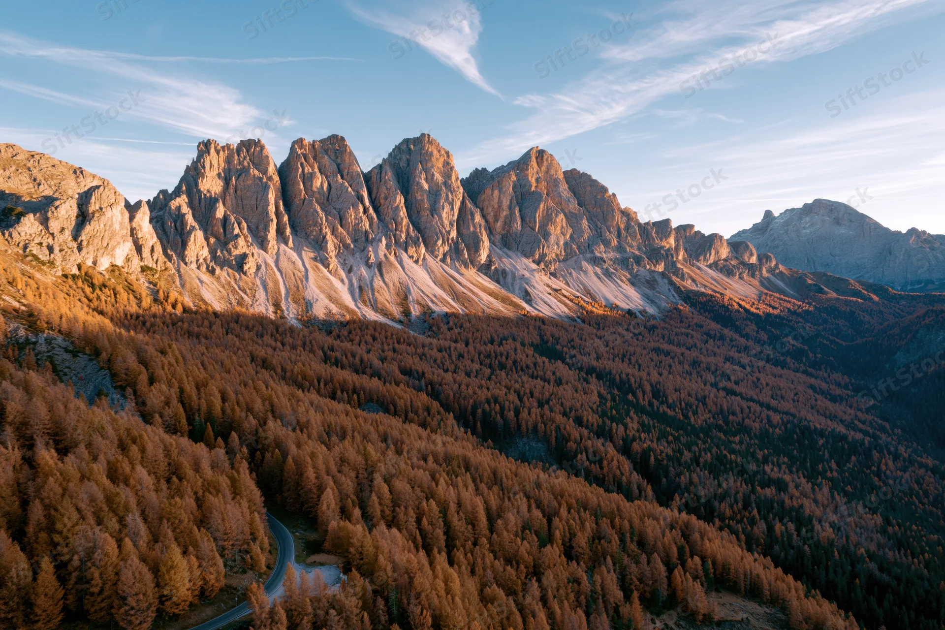 Jagged rocky peaks of the dolomites in autumn with golden larch forest and winding road below