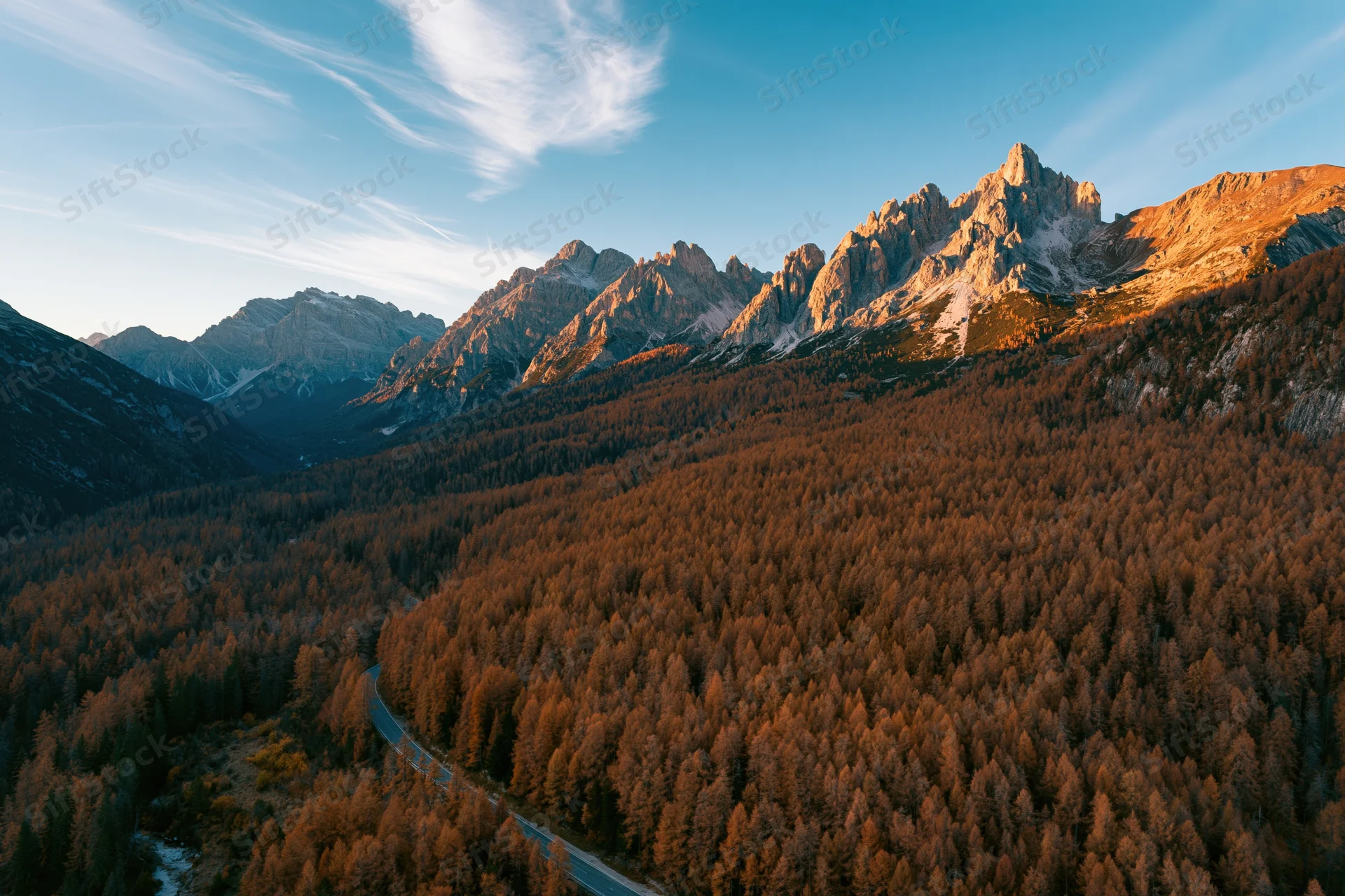 Aerial view of jagged dolomite peaks above autumn forest valley with winding road