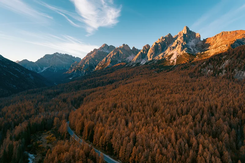 Aerial view of jagged dolomite peaks above autumn forest valley with winding road