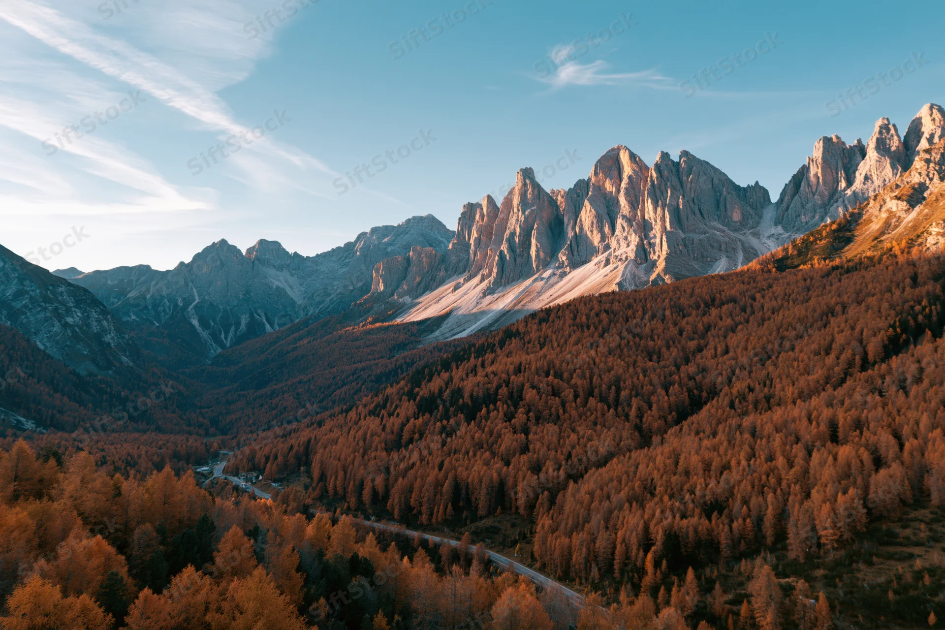 Aerial view of jagged dolomite peaks above autumn-colored larch forest in valley