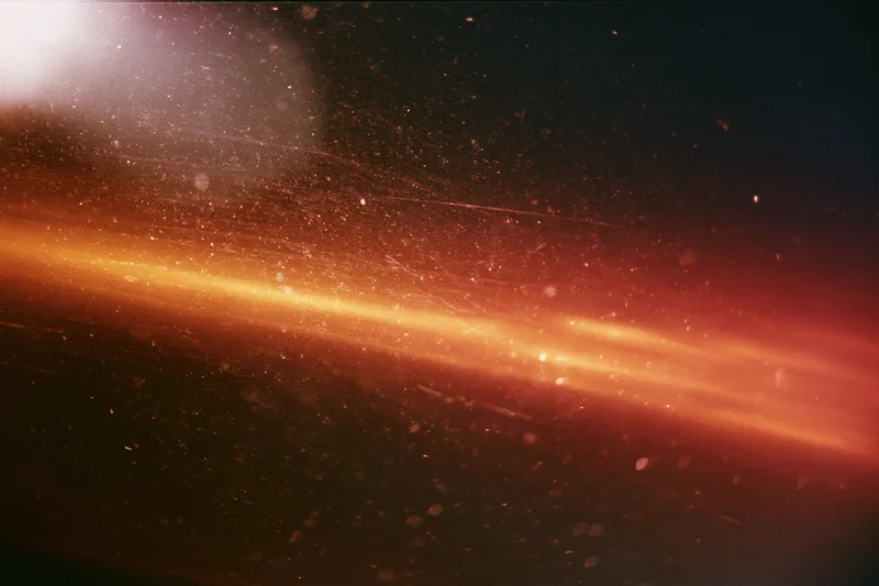 Warm light leak bleeding across dark analog film frame with visible grain and floating particles