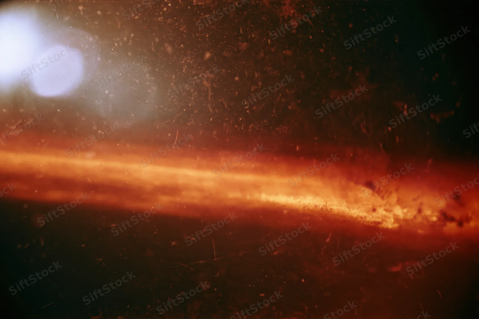 Aged analog film frame with orange light leak bleeding across the center, showing grain and dust particles in the dark background