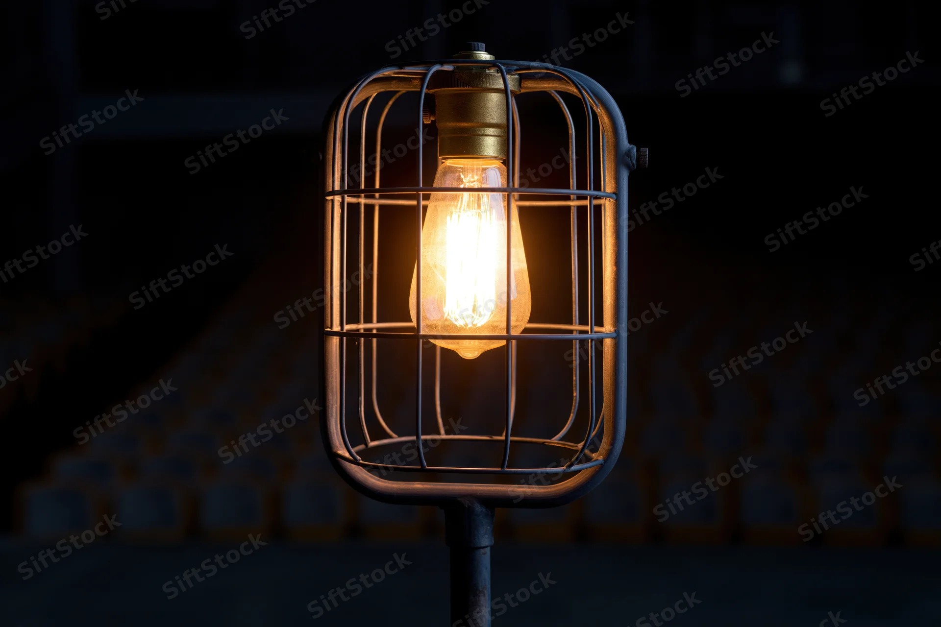 Industrial cage light with glowing Edison bulb on metal stand in dark setting