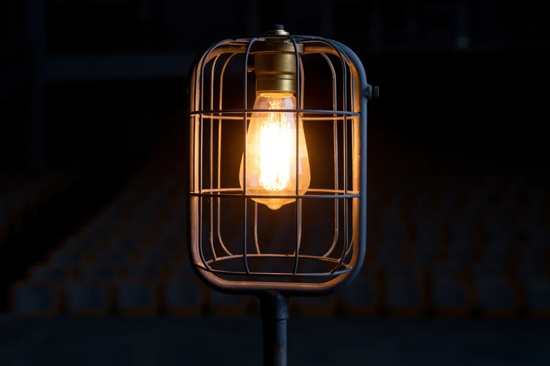 Industrial cage light with glowing Edison bulb on metal stand in dark setting