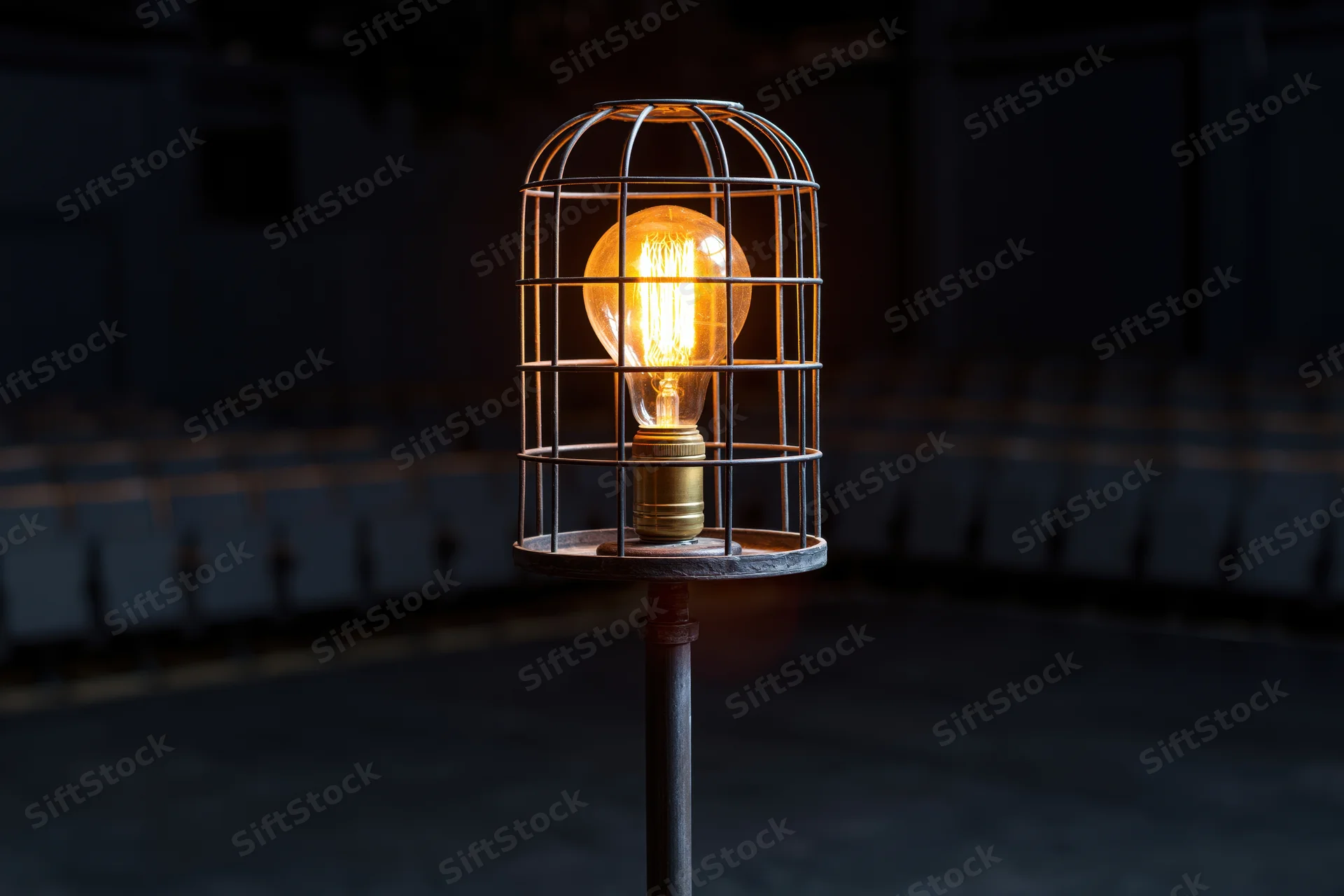 Industrial cage work light glowing warmly on metal stand in dark space