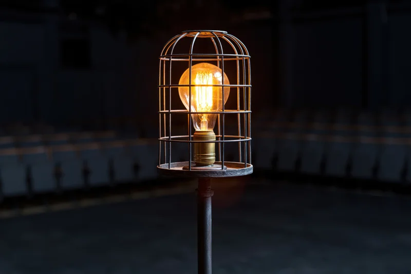 Industrial cage work light glowing warmly on metal stand in dark space