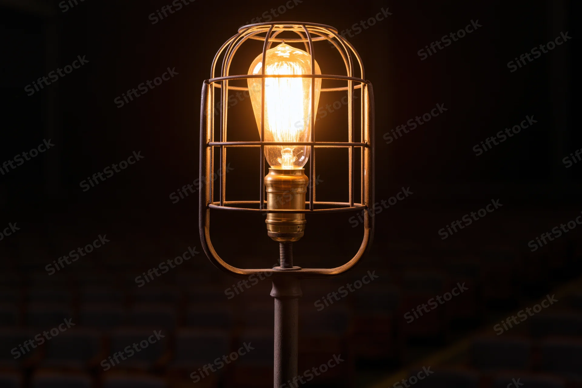 Industrial cage work light glowing warmly on metal stand in dark interior