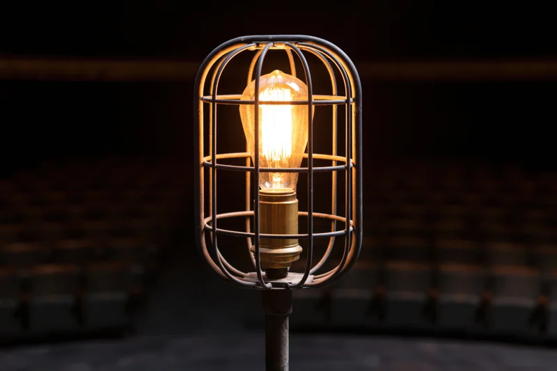 Industrial cage work light glowing warmly on metal stand in dim interior