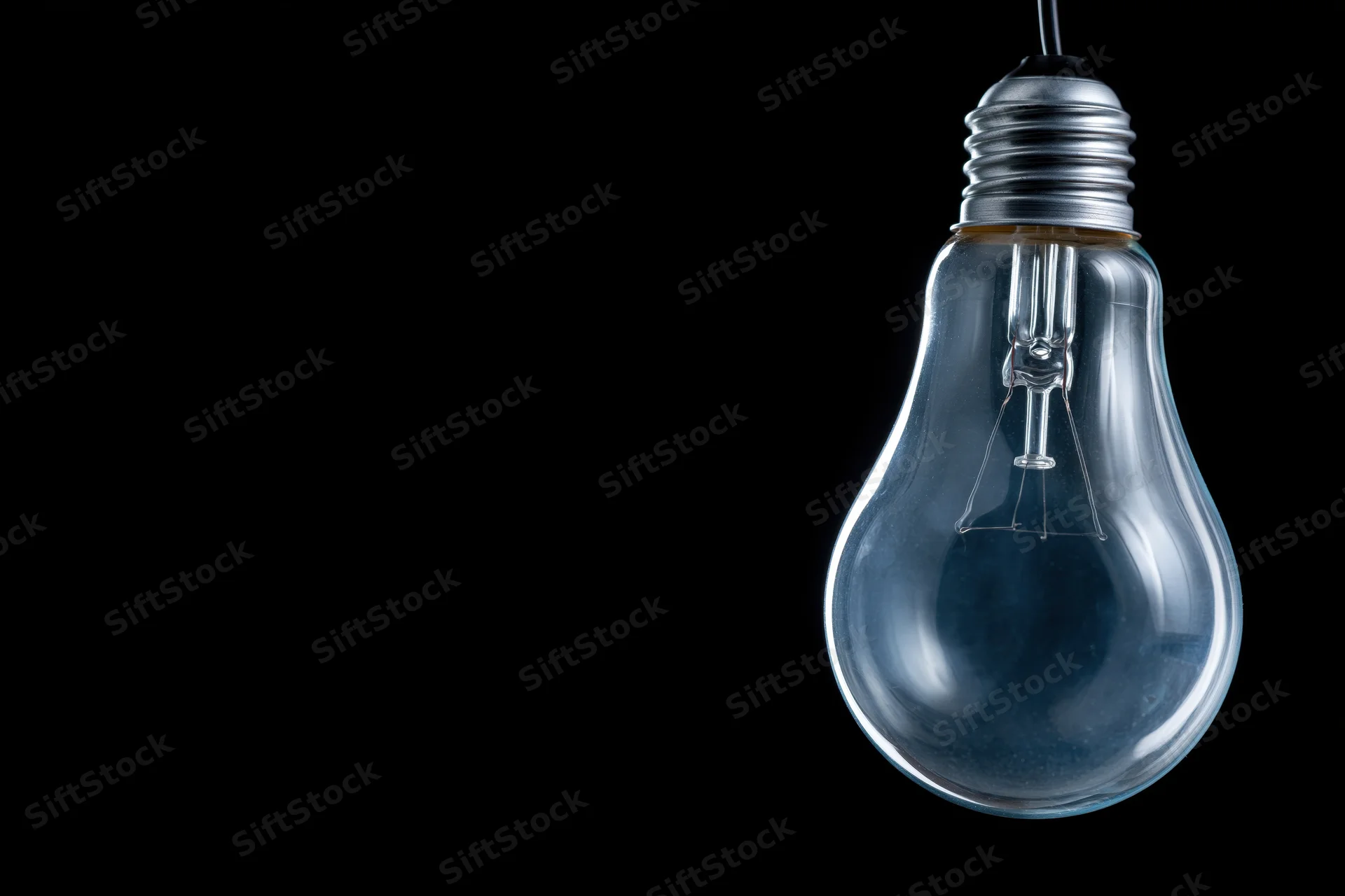 Unlit clear glass incandescent light bulb hanging from a wire against black background with copyspace