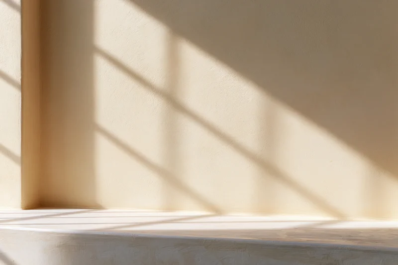 Beige plaster wall with diagonal sunlight shadow from window blinds in interior corner