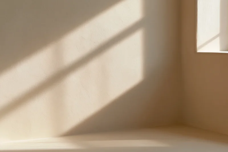 Diagonal sunlight casting soft shadow on beige plaster wall in interior corner