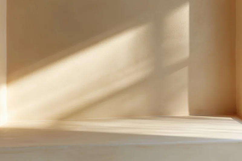 Beige plaster wall with diagonal sunlight shadow from window in interior corner