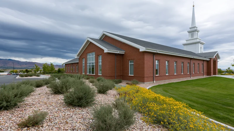 Brick lds meetinghouse with white steeple and landscaped grounds under cloudy sky