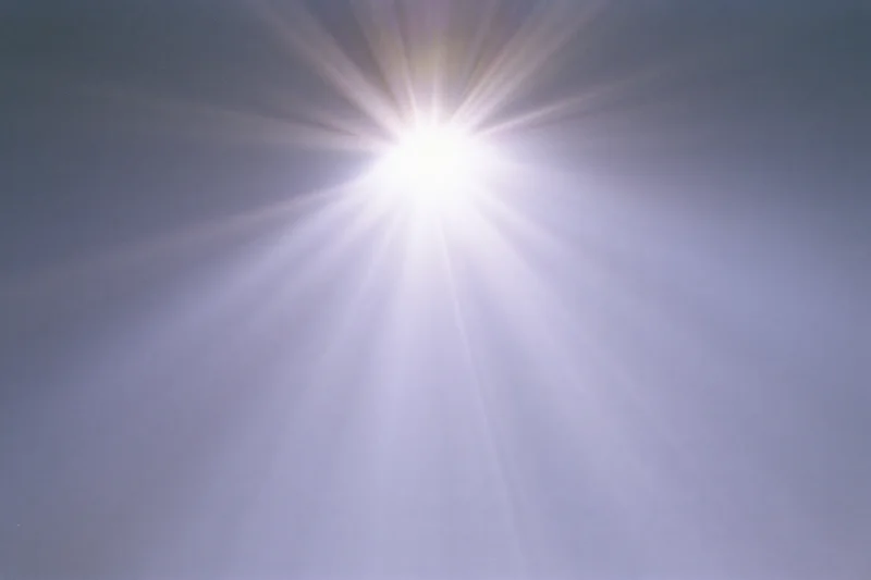 Bright lens flare burst radiating downward rays across a plain sky