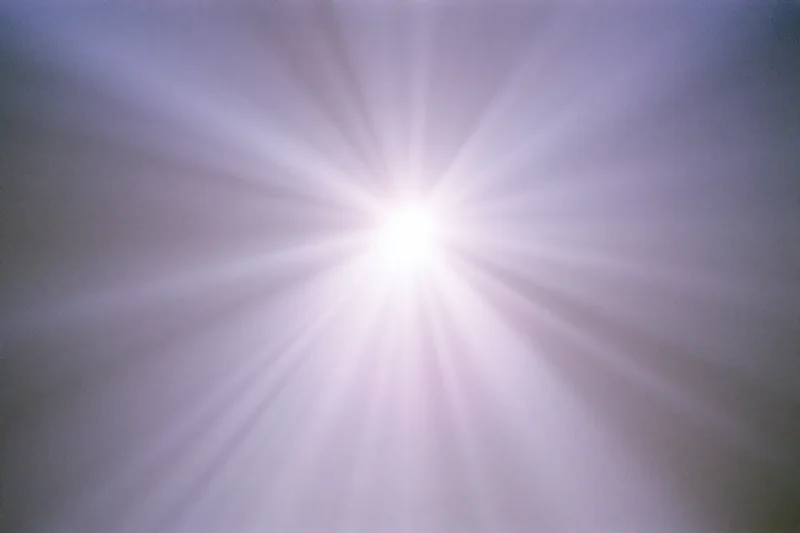 Bright lens flare burst radiating downward rays across a plain background