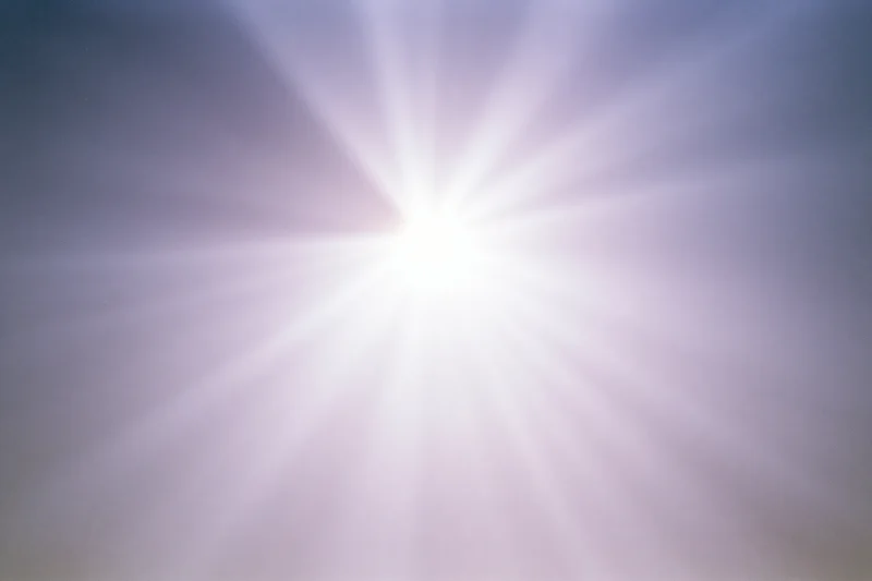 Bright lens flare burst radiating downward rays across a plain gradient background