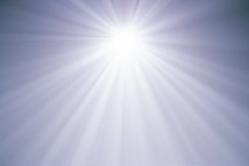Bright lens flare burst radiating downward rays across a plain background