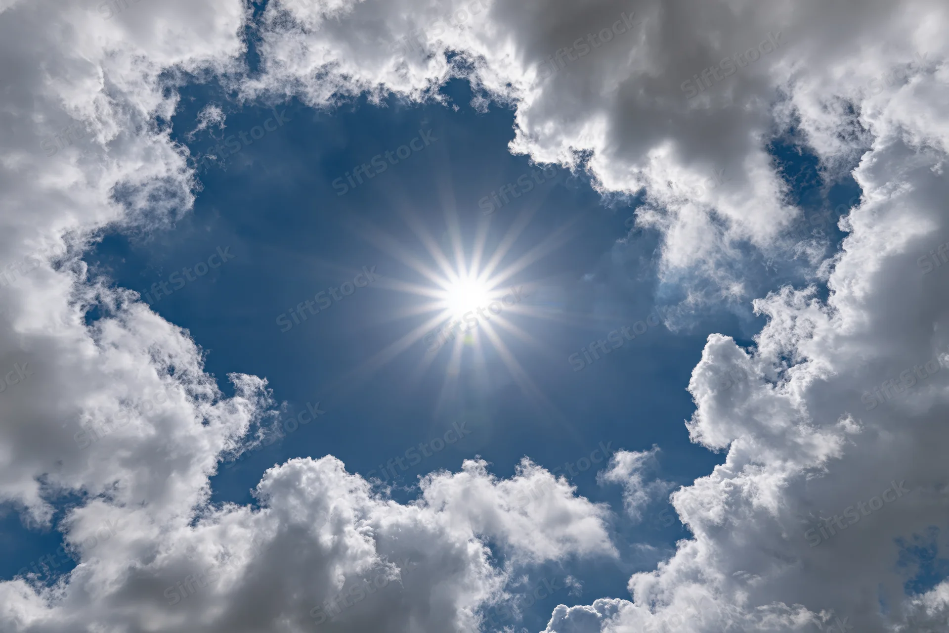 Bright sun bursting through a break in white cumulus clouds against a blue sky