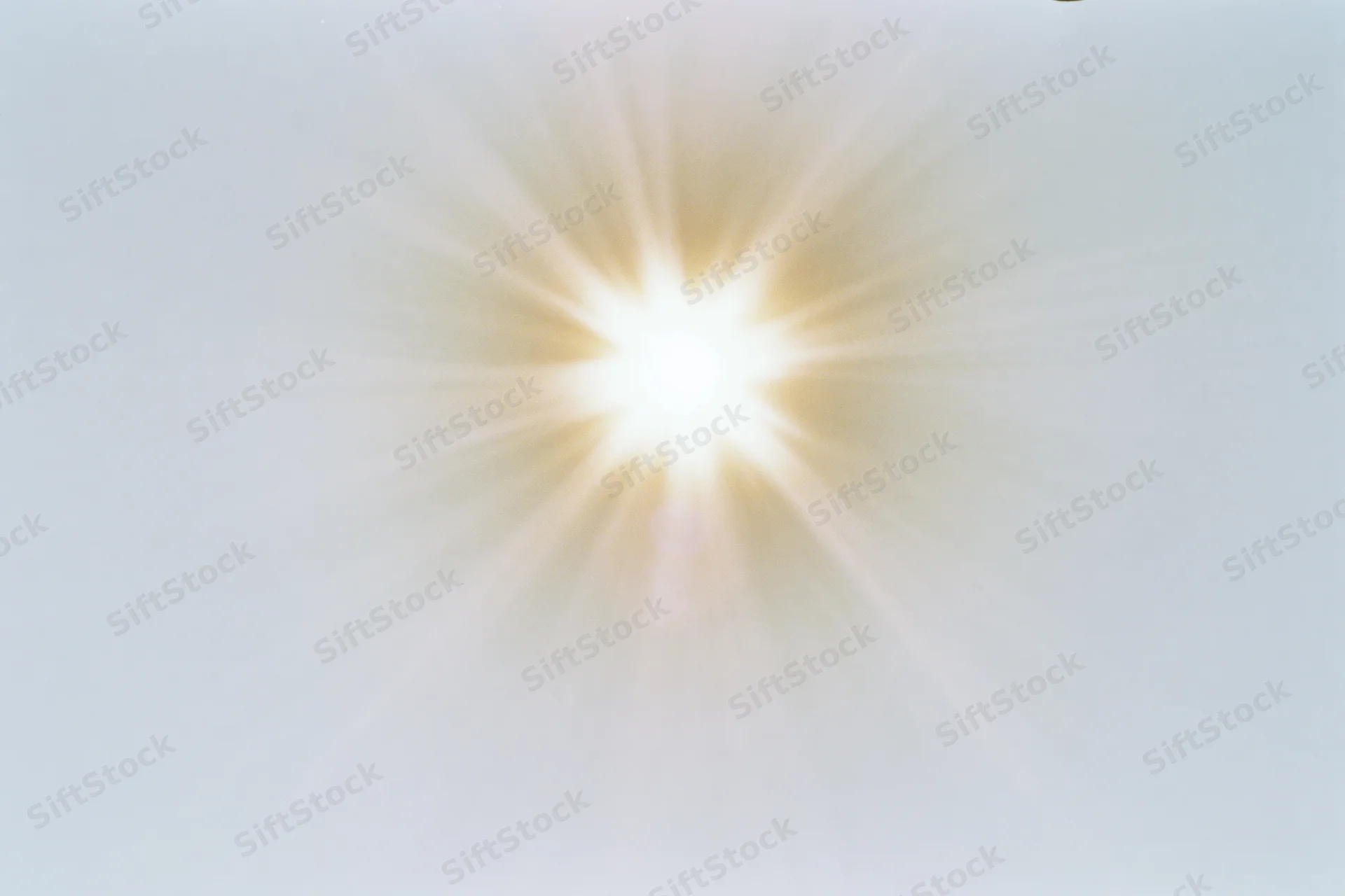 Bright midday sun radiating light against a pale white sky