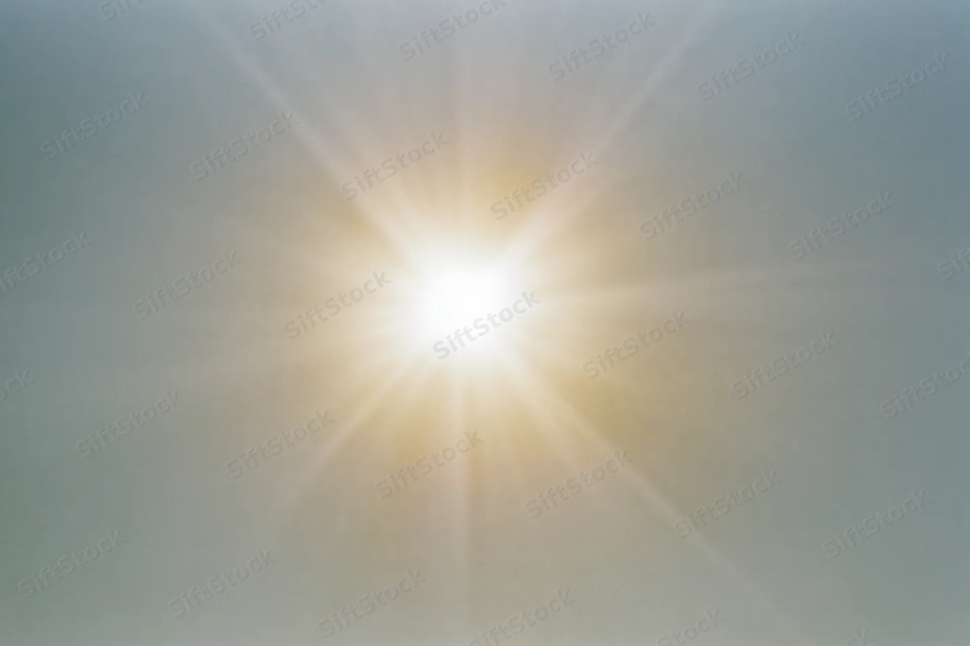 Bright midday sun shining in pale sky with lens flare and radiating light beams