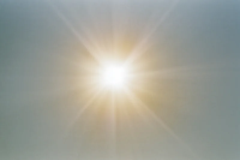 Bright midday sun shining in pale sky with lens flare and radiating light beams