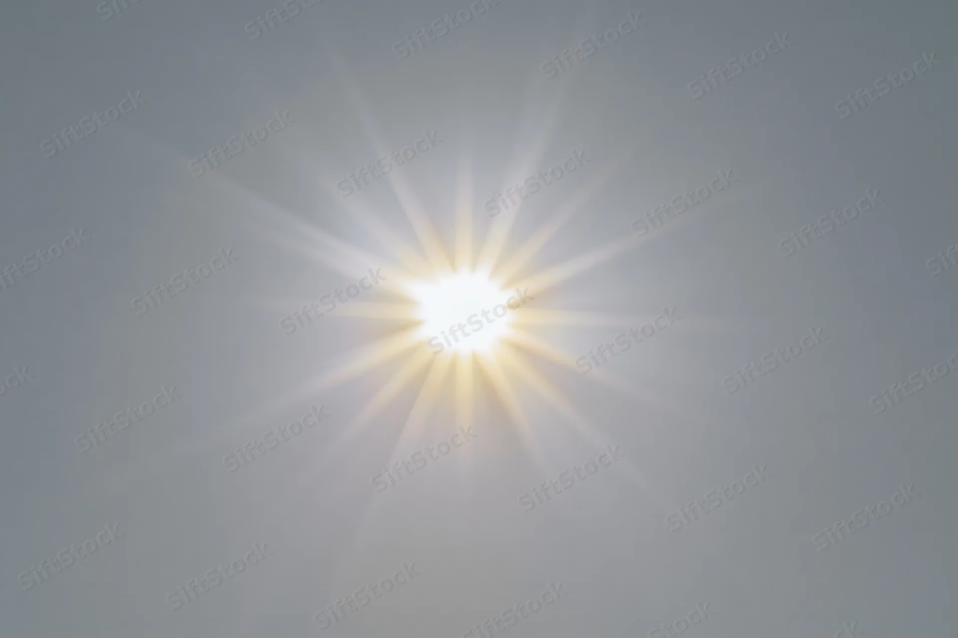 Bright sun burst with radiating light rays centered on a plain sky background