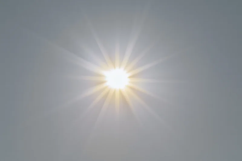 Bright sun burst with radiating light rays centered on a plain sky background