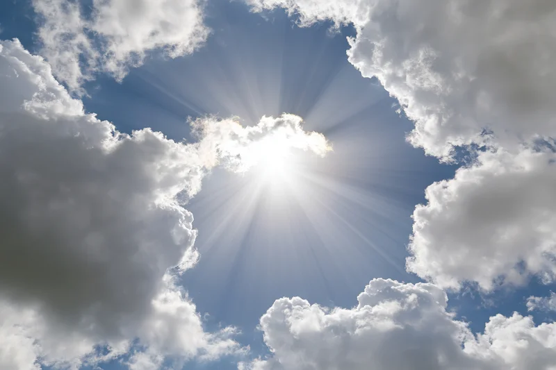 Sun bursting through a break in white cumulus clouds against a blue sky