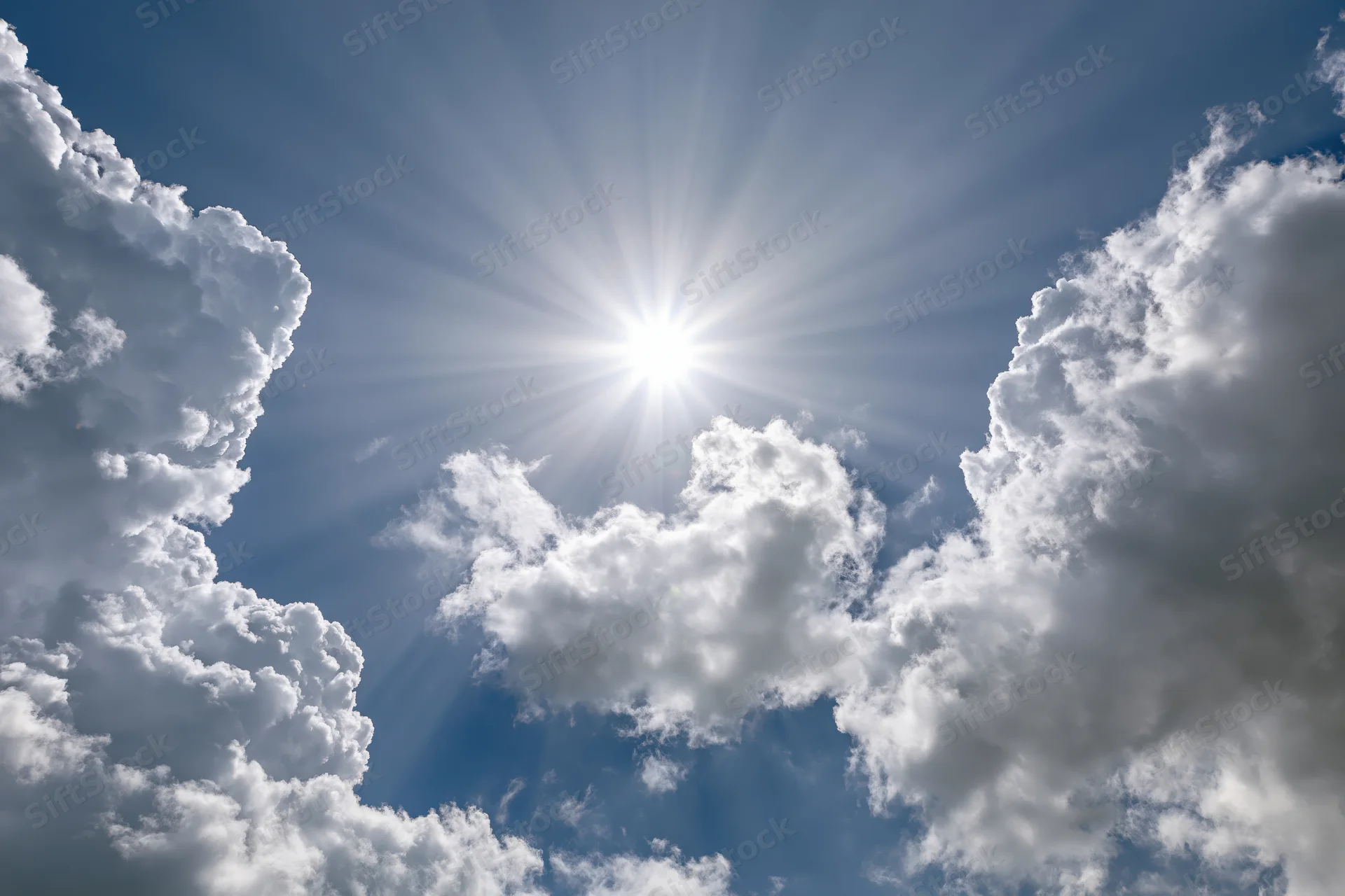 Bright sun bursting through a break in white cumulus clouds against a blue sky