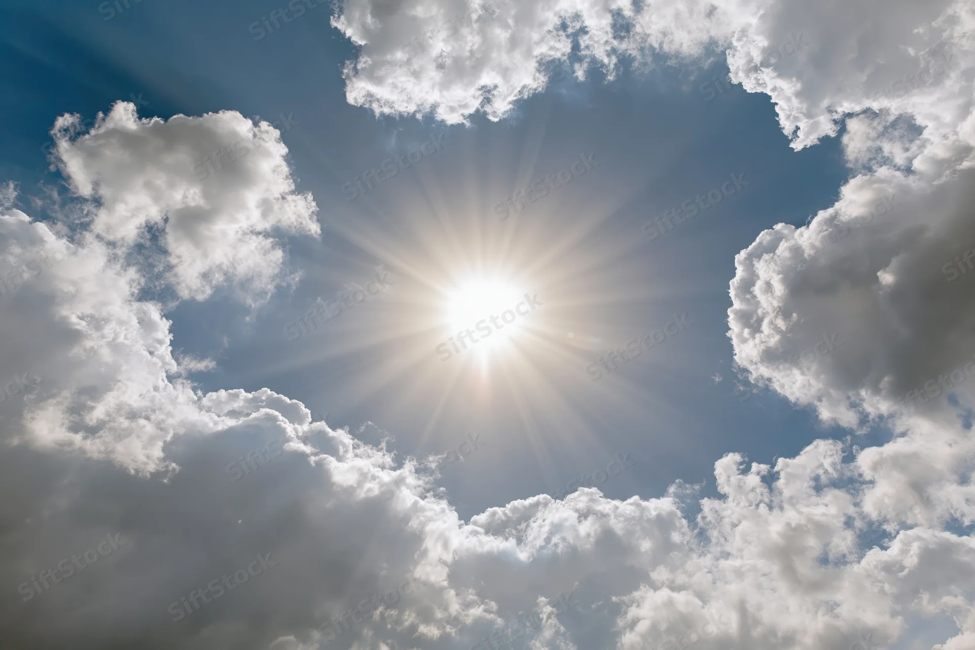 Bright sun bursting through a break in white cumulus clouds against a blue sky