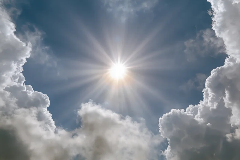 Bright sun bursting through a break in white cumulus clouds against a blue sky