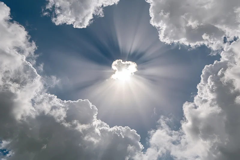 Sun bursting through a break in white cumulus clouds against a blue sky