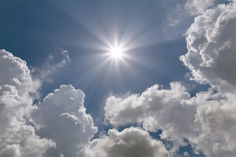 Bright sun bursting through a break in white cumulus clouds against a blue sky