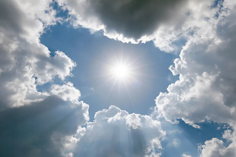 Bright sun bursting through gap in white cumulus clouds against blue sky