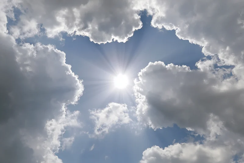 Bright sun bursting through a gap in white cumulus clouds against a blue sky