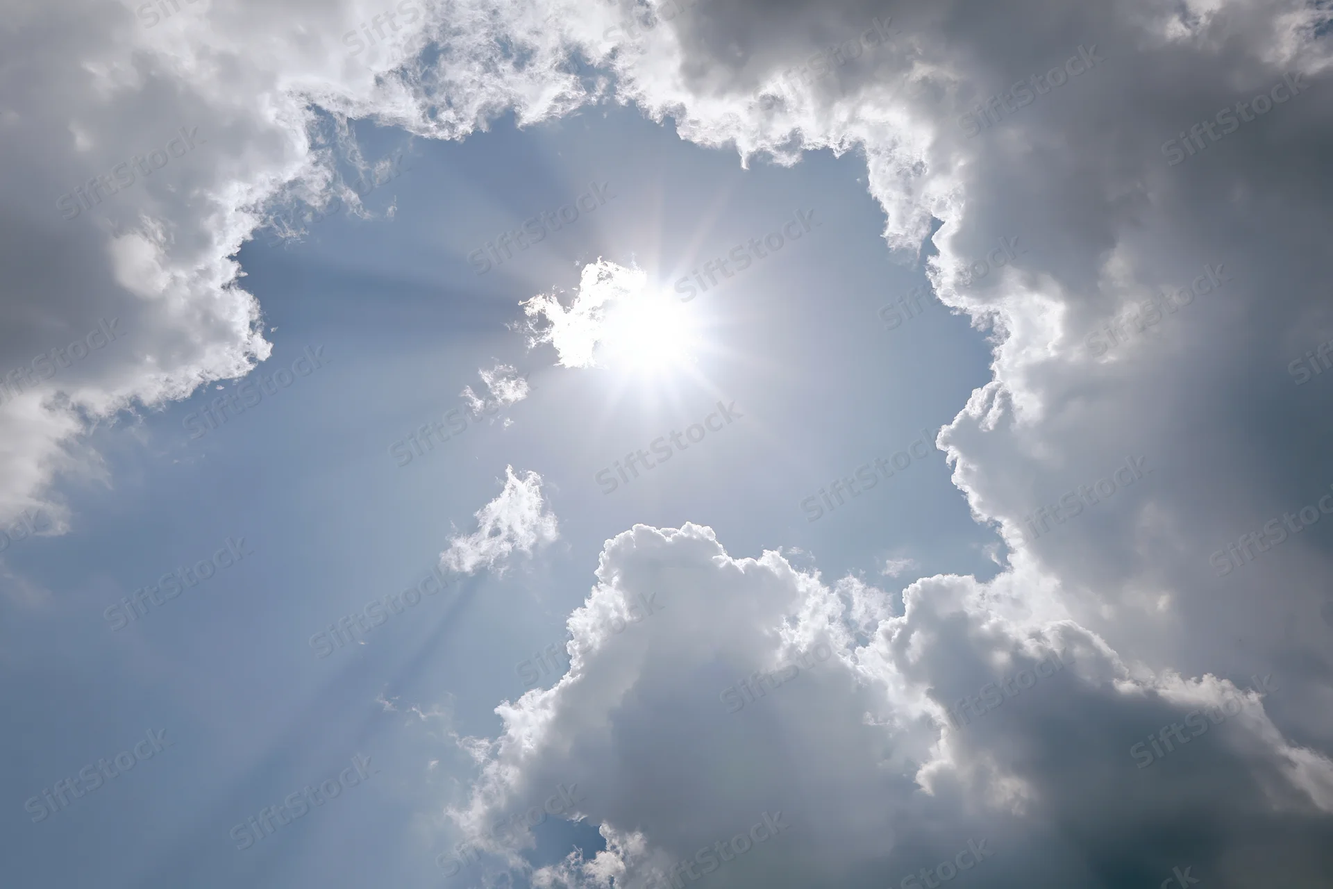 Bright sun bursting through a gap in white cumulus clouds against a blue sky