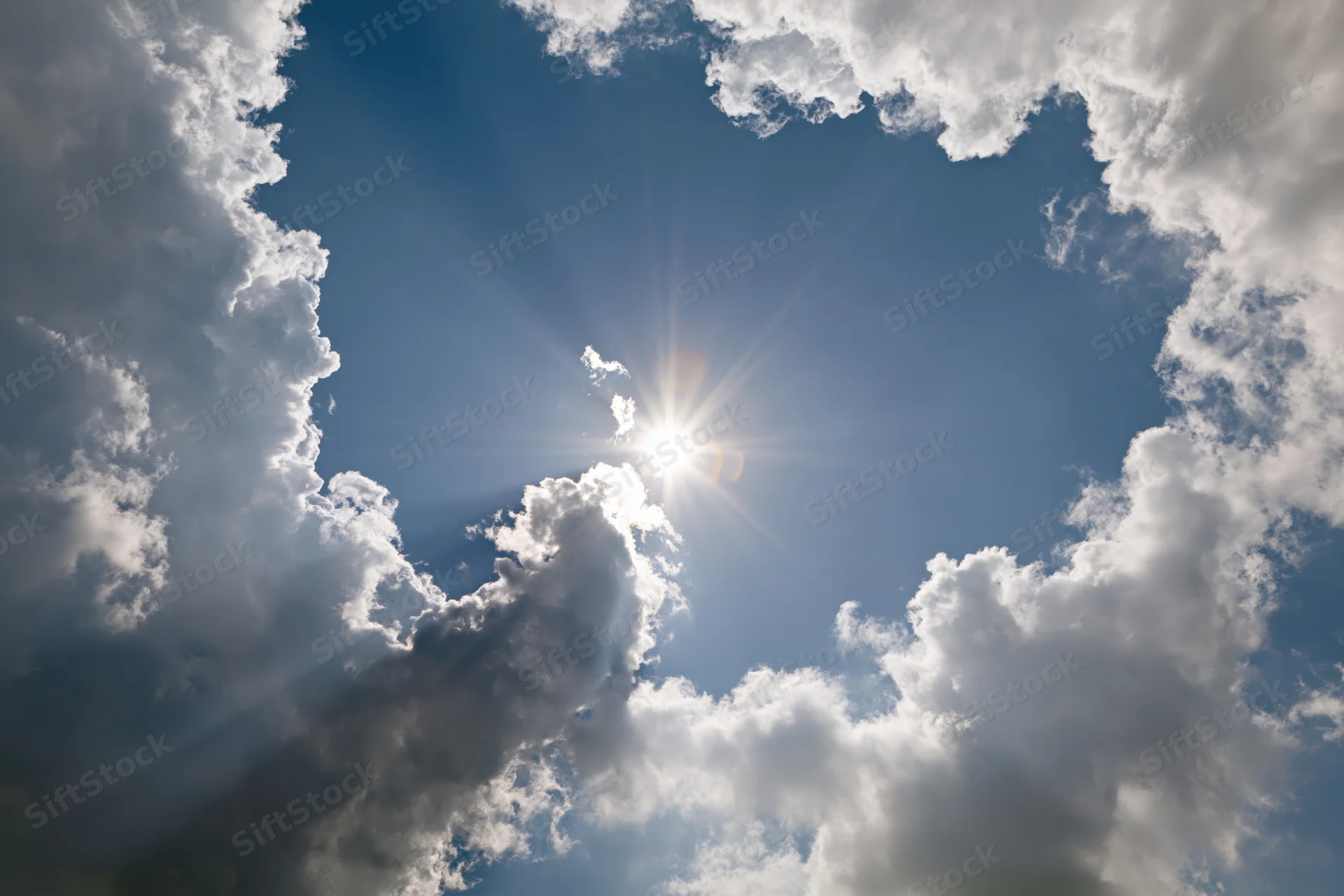 Bright sun bursting through gap in white cumulus clouds against blue sky