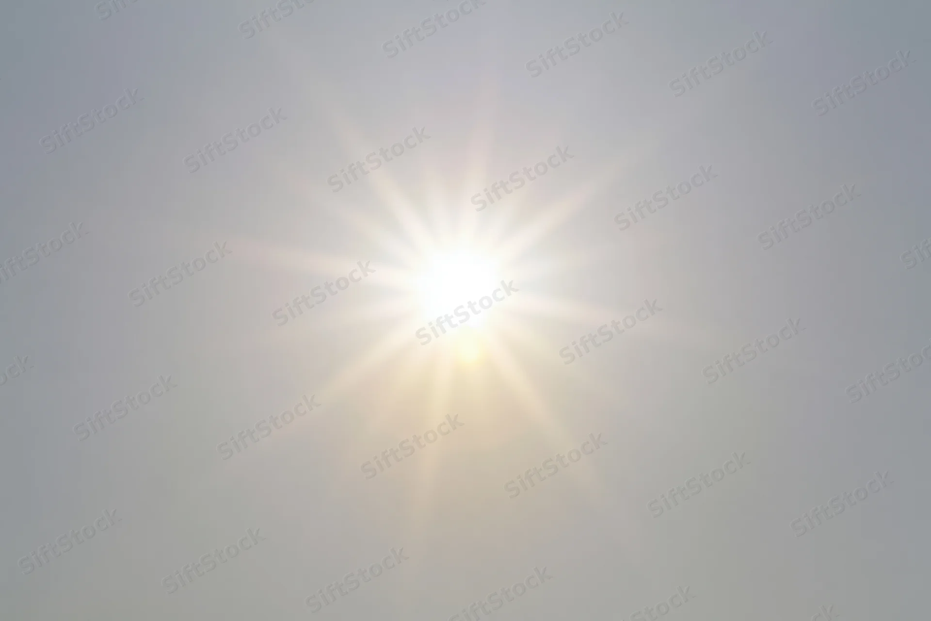 Bright sunburst lens flare radiating light rays from center against hazy sky